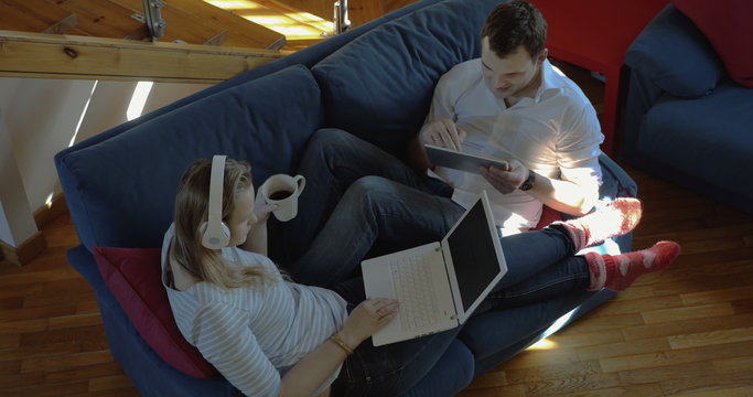 Man and woman at home using pad and laptop