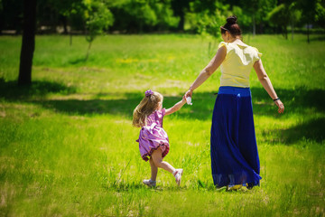 Naklejka na ściany i meble Little girl together with mother run and play on a grass in the