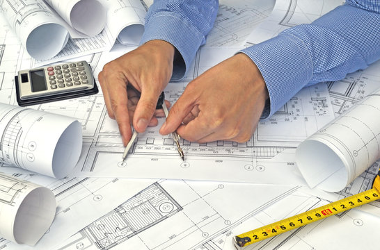 Hands of engineer working with the tool on project drawings background