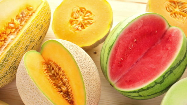 Variety of organic melons sliced on wood table.