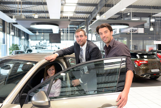 Verkäufer im Autohandel berät junges Paar beim Kauf eines Neuwagens // Couple at car dealership