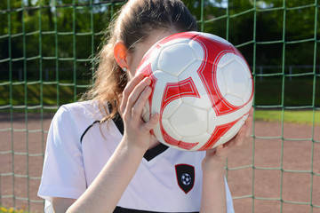 Mädchen beim Frauenfußball hält Lederfußball vor Kopf 