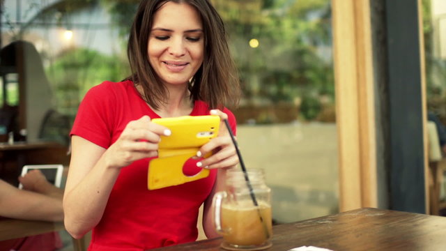 Young, pretty woman talking photo of drink with cellphone sitting in cafe 
