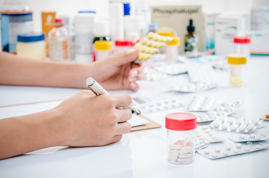pharmacist holding medicine tablet and writing prescription 
