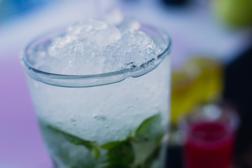 Beautiful line of different colored alcohol mojito cocktails with mint on a open air party, tequila, martini, vodka, and others on decorated catering bouquet table on open air event party.