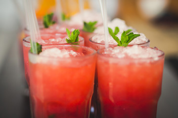Beautiful line of different colored alcohol mojito cocktails with mint on a open air party, tequila, martini, vodka, and others on decorated catering bouquet table on open air event party.