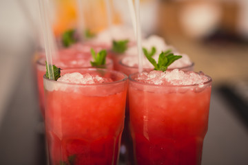 Beautiful line of different colored alcohol mojito cocktails with mint on a open air party, tequila, martini, vodka, and others on decorated catering bouquet table on open air event party.
