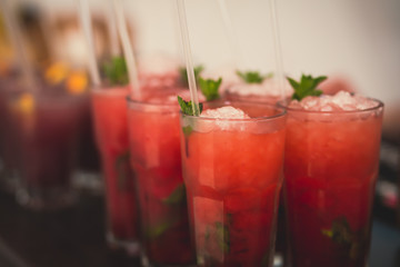 Beautiful line of different colored alcohol mojito cocktails with mint on a open air party, tequila, martini, vodka, and others on decorated catering bouquet table on open air event party.