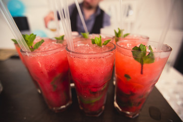 Beautiful line of different colored alcohol mojito cocktails with mint on a open air party, tequila, martini, vodka, and others on decorated catering bouquet table on open air event party.