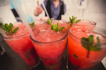Beautiful line of different colored alcohol mojito cocktails with mint on a open air party, tequila, martini, vodka, and others on decorated catering bouquet table on open air event party.