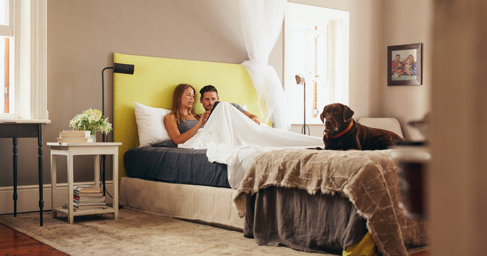 Young Couple Sharing A Digital Tablet While Relaxing In Bed