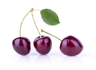 Three ripe cherries with leaves on a white background
