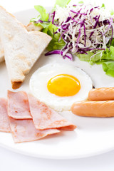 Plate of breakfast with fried eggs, toast, ham, sausage and vegetables on white background