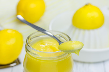 Lemon curd in a glass jar with fresh lemons on background
