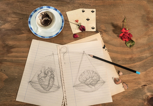   Tazzina  vuota con fondo di caff&egrave; in forma di cuore,petali di rosa secchi,matita e disegno di cuore e cervello sulla bilancia.
