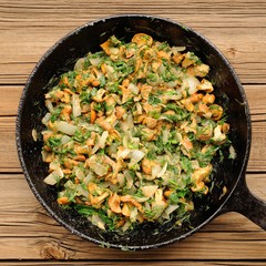Fried chanterelle mushrooms with greens in black cast iron pan