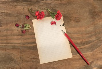 Rose rosse con foglio bianco e penna rossa su tavolo di legno grezzo.

