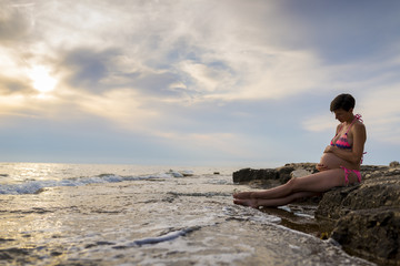 Pregnant woman in ninth month of pregnancy sitting on a rock by