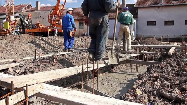 Team of construction workers are working on concreting at construction site. Construction workers are pulling large hose for concreting of steel reinforced concrete on construction site.