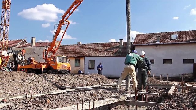 Team of construction workers are working on concreting at construction site. Construction workers are pulling large hose for concreting of steel reinforced concrete on construction site.