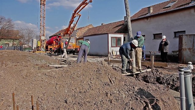 Team of construction workers are working on concreting at construction site. Construction workers are pulling large hose for concreting of steel reinforced concrete on construction site.