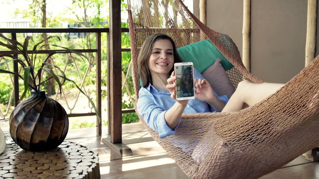 Young woman taking selfie photo with cellphone lying on hammock

