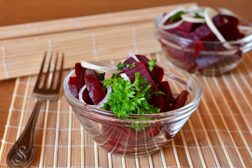 Fresh sliced beetroot salad with onion and parsley on a glass bowl on a table