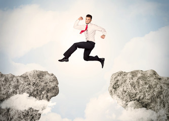 Happy business man jumping over a cliff