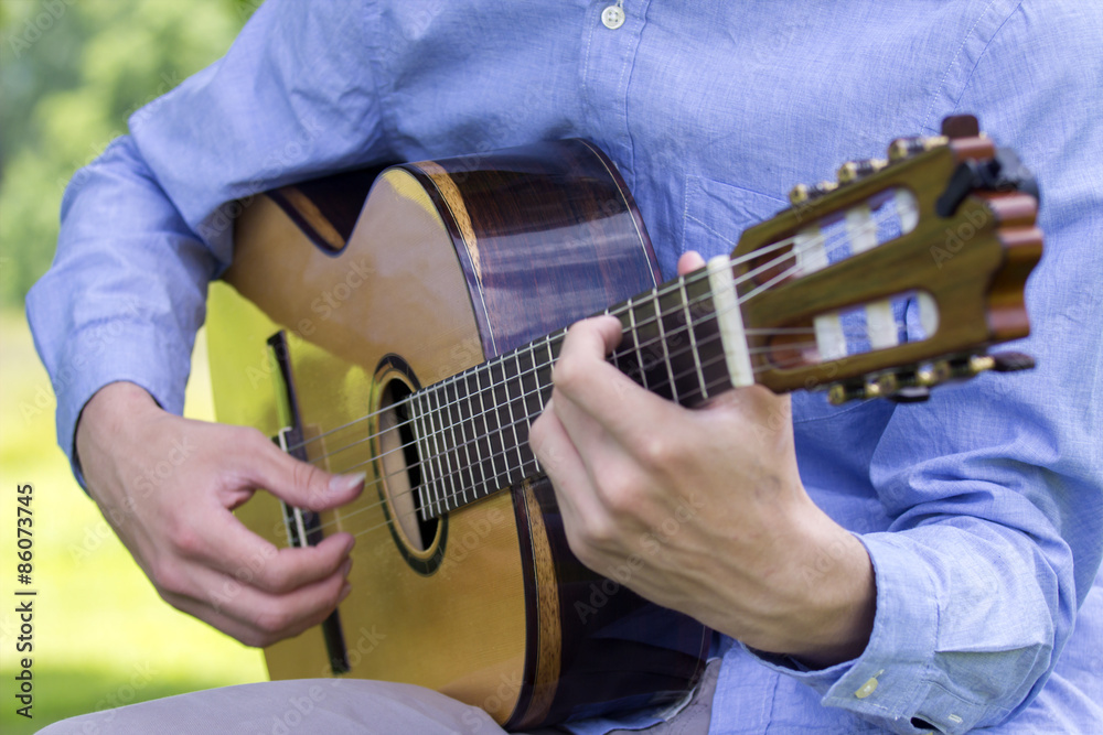 Wall mural young male playing a classic guitar outside