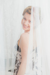 Smiling woman  behind  white transparent textile © OlgaKhorkova