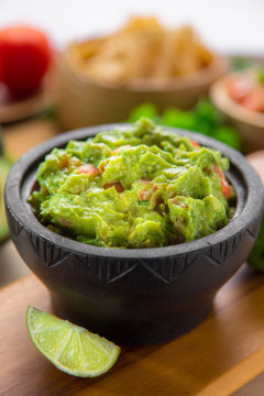 Clean vertical shot of a fresh bowl of guacamole and restaurant style tortilla chips