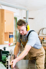 Schreiner oder Tischler beim Sägen einiger Bretter mit einer elektrischen Kreissäge in einer Tischlerei oder Werkstatt, er trägt Gehörschutz und Schutzbrille für die Arbeitssicherheit