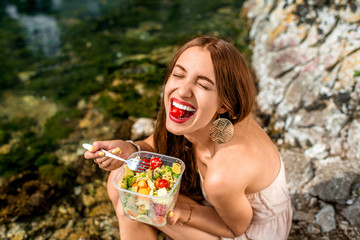 Woman eating healthy salad near the river - obrazy, fototapety, plakaty
