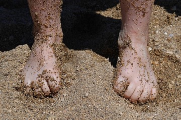 Feet of 5 years old boy with flexed fingers covered with sand on beach
