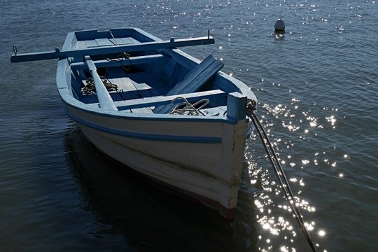 Blue and white tall wooden fishing boat anchored with rope, buoy in background