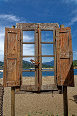 Blick durch ein altes Fenster, im Hintergrund eine Bucht nit Wasser und Bergen auf Korsika