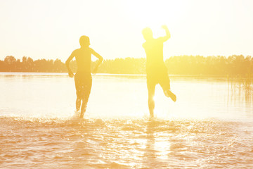 Glückliche junge Menschen laufen und springen am See beim Sonnenuntergang