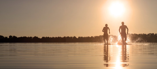 Glückliche junge Menschen laufen und springen am See beim Sonnenuntergang