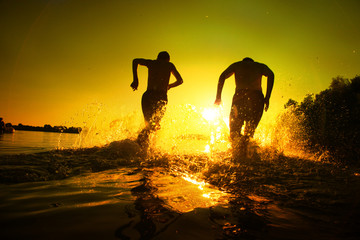 Glückliche junge Menschen laufen und springen am See beim Sonnenuntergang