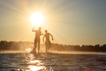 Glückliche junge Menschen laufen und springen am See beim Sonnenuntergang