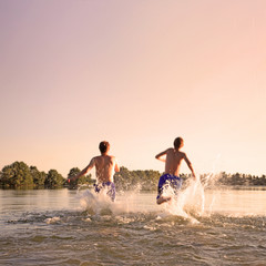 Glückliche junge Menschen laufen und springen am See beim Sonnenuntergang