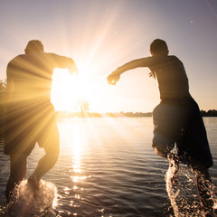 Glückliche junge Menschen laufen und springen am See beim Sonnenuntergang © Thaut Images