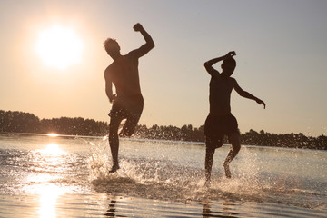 Glückliche junge Menschen laufen und springen am See beim Sonnenuntergang