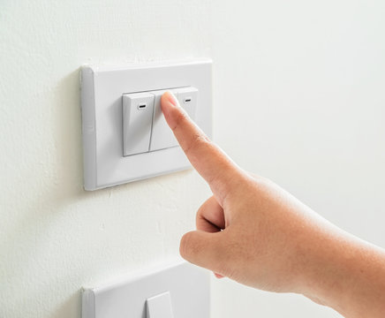 Womans hand with finger on light switch to turn off the lights.