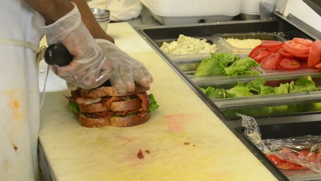 Chef slicing a BLT sandwich in a restaurant kitchen
