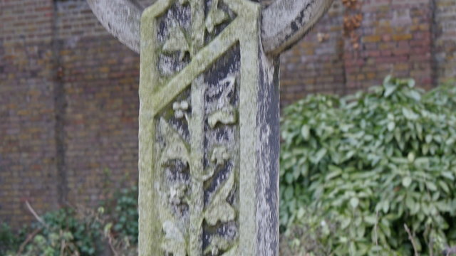 Cement carved into a big cross found in the London cemetery. Seen in the background is a big wall and some green plants
