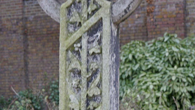 Big old cement cross in London cemetery. It has little moss in it with grasses on the bottom