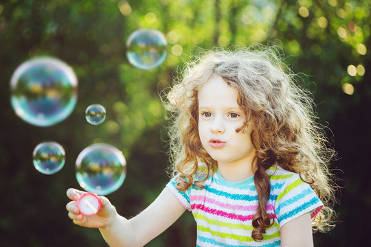 Cute girl blowing soap bubbles, closeup portrait.