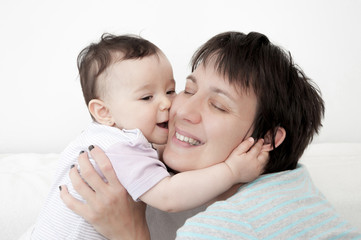 Baby girl kissing her loving mother. They are hugging each other. High key