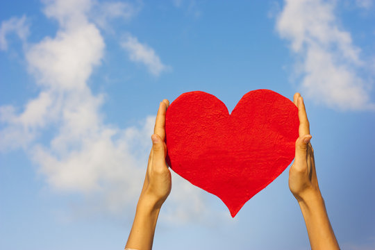 Paper red heart in hand on the sky background